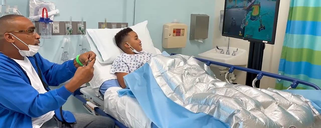 A father at his son's hospital bedside while the boy plays a racing game