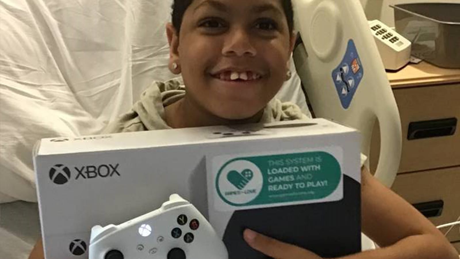 A child in a hospital bed smiling with a new Xbox console from Games For Love